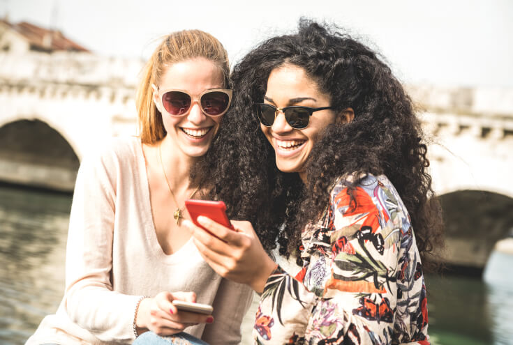 Happy multiracial girlfriends having fun outddors with mobile smart phone - Friendship concept with girls at spring break travel - Modern female lifestyle with women best friends - Bright filter tone