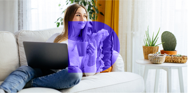 Woman sitting on the couch holding coffee and a laptop